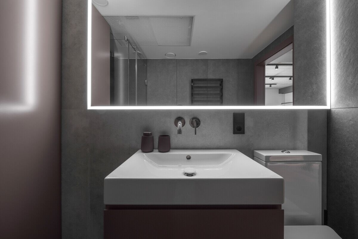 Modern minimalist bathroom interior design with grey stone tiles and over mirror lighting
