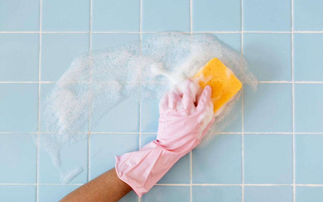 Pink gloved hand scrubbing bathroom tiles