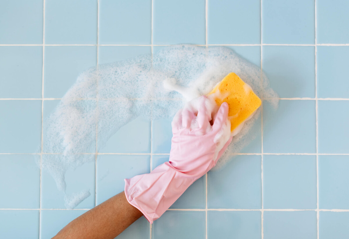 Pink gloved hand scrubbing bathroom tiles