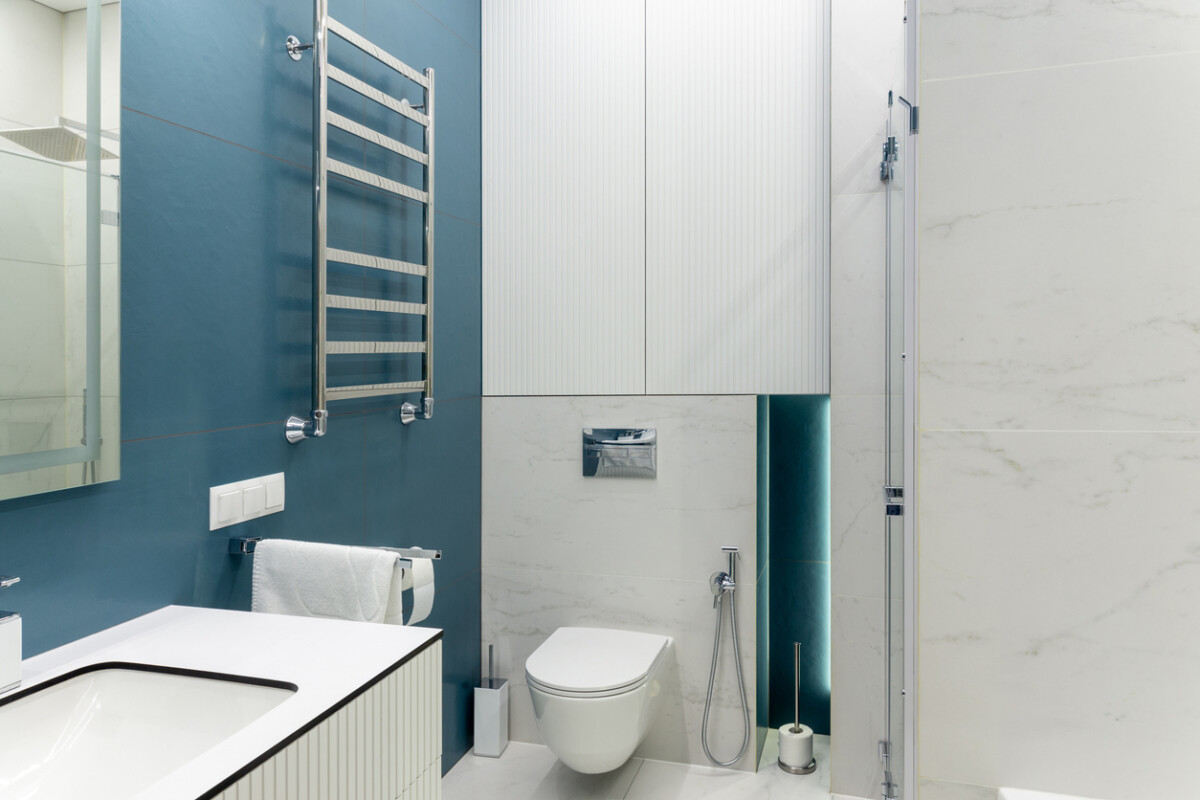 Blue and white bathroom with toilet, large mirror, shower, lighting, and basin. Spacious, clean, and luxurious.