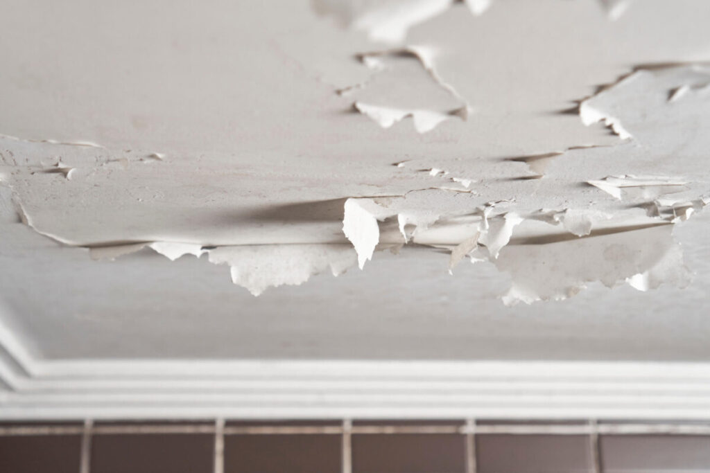 Damaged bathroom ceiling with cracked and peeling white paint on painted drywall close-up.
